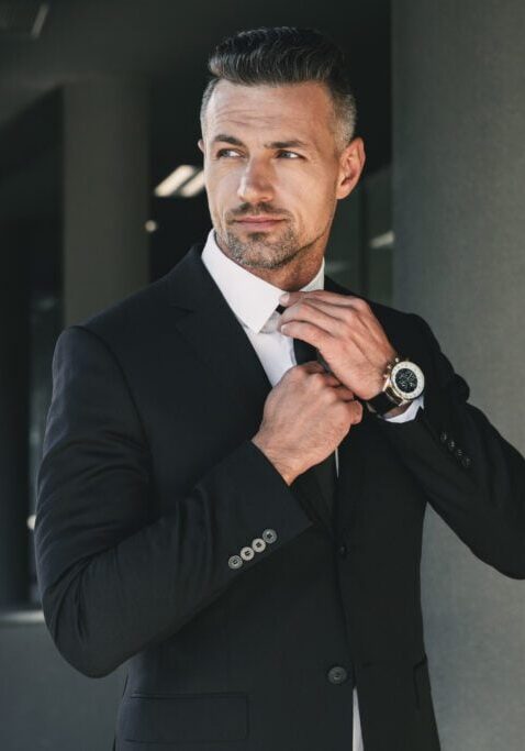 Portrait of a charming young businessman Portrait of a charming young businessman dressed in suit standing outside a glass building and touching his tie