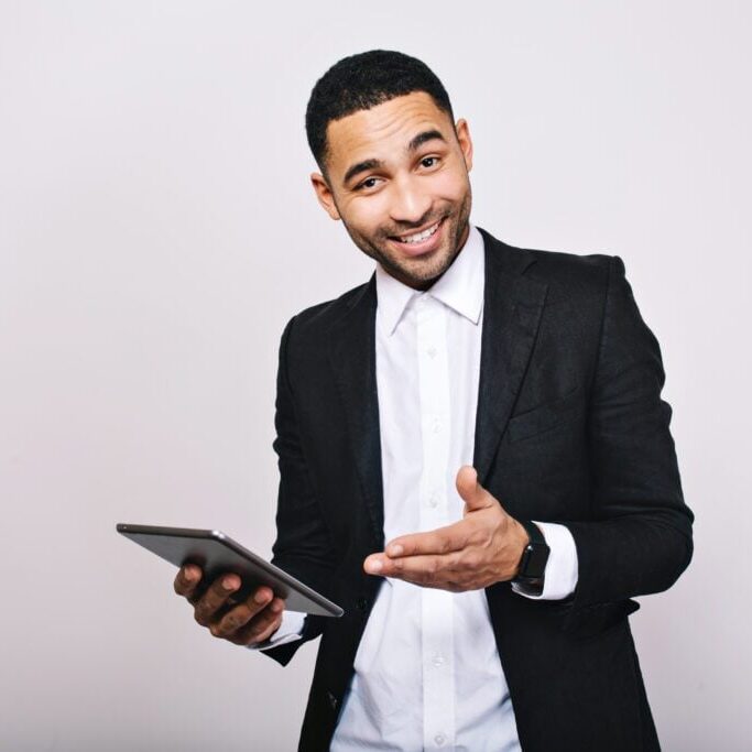 Stylish young handsome man in white shirt, black jacket, with tablet smiling to camera on white background. Achieve success, great work, expressing true positive emotions, businessman, smart worker